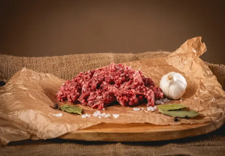 Świeże, mielone mięso wołowe, idealne na soczyste burgery. Obok czosnek, sól, liście laurowe i pieprz.