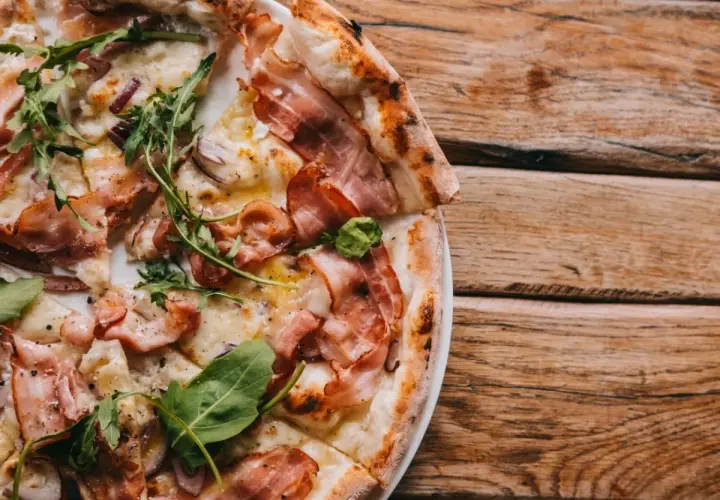 Pyszna pizza carbonara z chrupiącym boczkiem, rukolą i cebulą na drewnianym blacie.