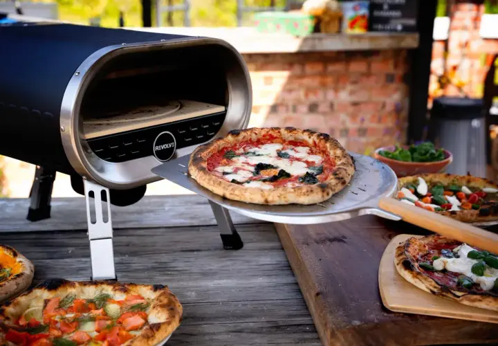 Piec do pizzy z otwartą komorą, na stole leżą świeżo upieczone pizze.
