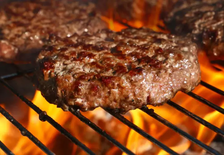 Soczyste kotlety mielone smażące się na grillu z płomieniami.