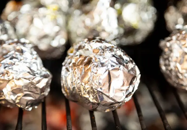 Ziemniaki z grilla zawinięte w folię aluminiową, piekące się nad żarem.