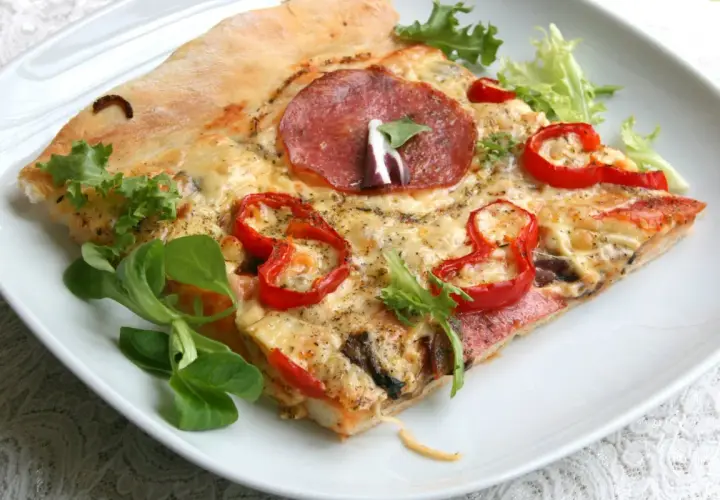 Kawałek pizzy z salami, papryką i serem na białym talerzu.