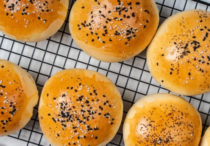 Złociste bułeczki do mini burgerów posypane sezamem i czarnuszką, na czarnej kratce.