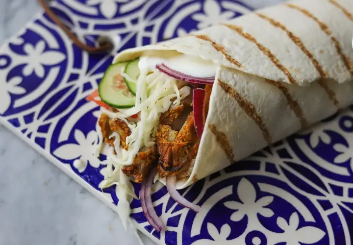 Pyszny kebab w picie z soczystym mięsem, chrupiącą kapustą, pomidorem, ogórkiem i czerwoną cebulą, podany na ozdobnym talerzu.