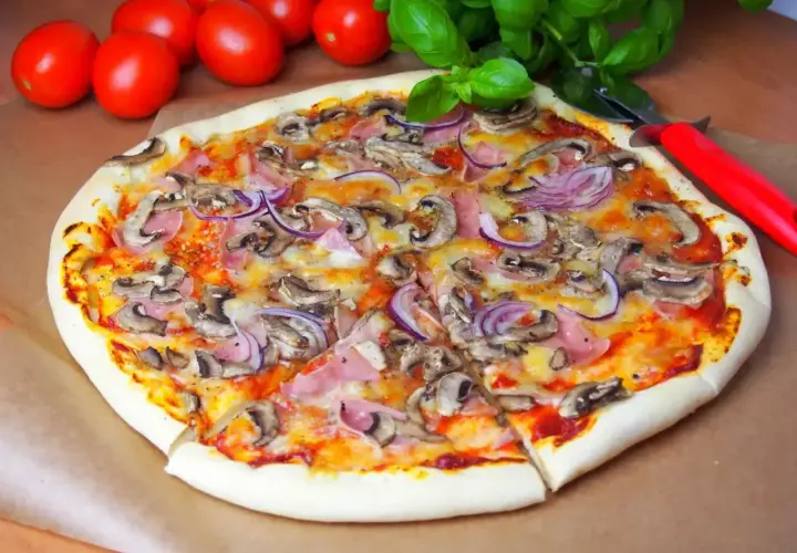 Pyszna pizza capriciosa z pieczarkami, szynką i czerwoną cebulą, gotowa do pokrojenia.