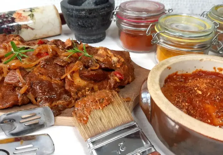 Karkówka na grilla w aromatycznej marynacie, gotowa do pieczenia. Obok pędzel z marynatą, przyprawy i narzędzia.