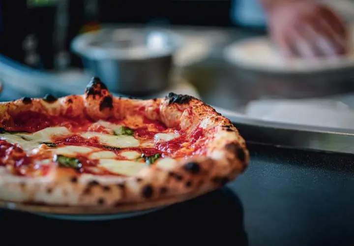 Puszysta pizza z serem i bazylią na ciemnym tle.