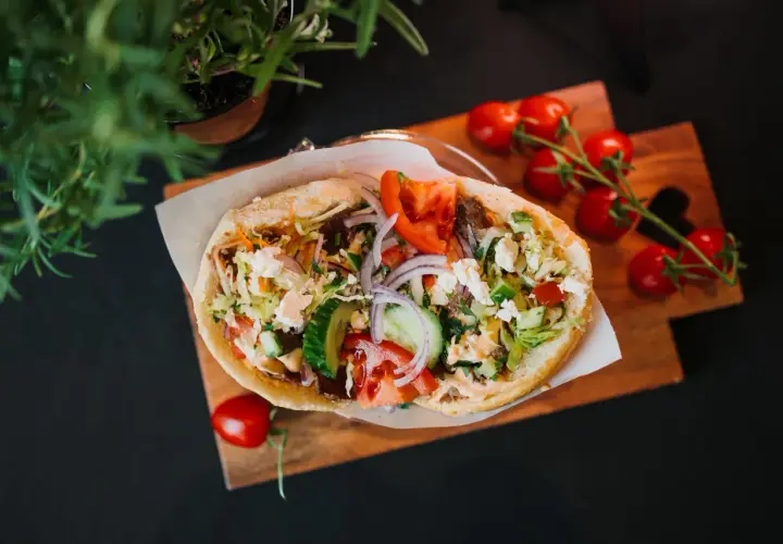 Pyszny kebab z warzywami i serem feta na desce, obok pomidorki i zielenina.