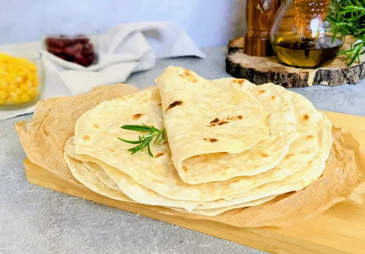 Stos świeżo upieczonych tortilli, idealnych do przygotowania najlepszej tortilli z ulubionymi dodatkami. Gałązka rozmarynu dodaje aromatu.