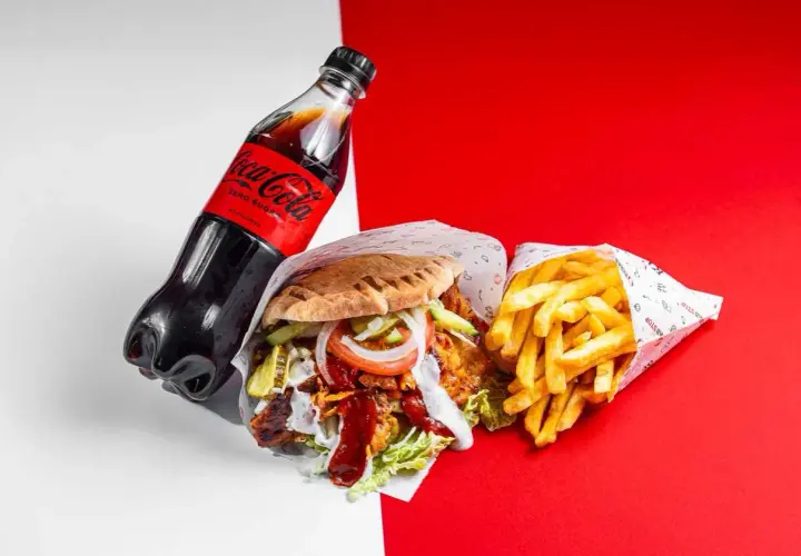 Duży kebab z frytkami i butelką Coca-Coli Zero na czerwono-białym tle.