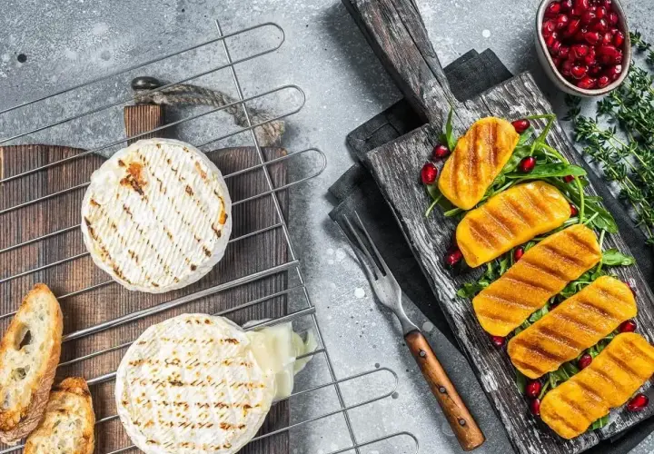 Dwa krążki sera camembert na grillu, jeden lekko roztopiony, obok grzanki i grillowane kawałki dyni z pestkami granatu.