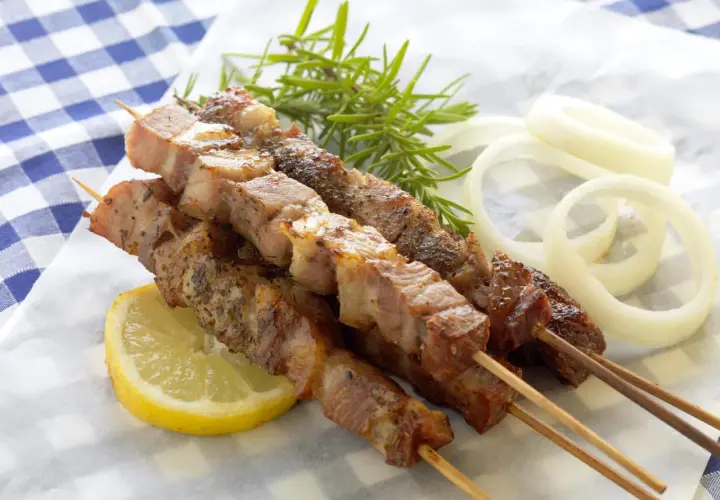 Aromatyczne souvlaki na patyczkach, podane z plasterkiem cytryny, gałązką rozmarynu i krążkami cebuli.
