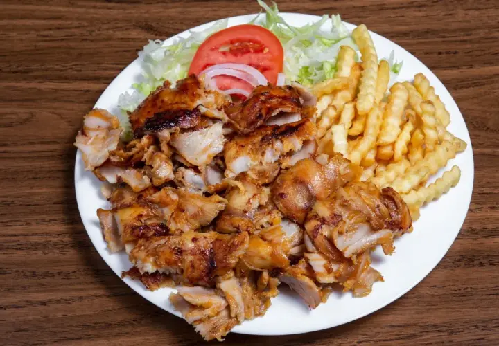Talerz z kurczakiem gyros, frytkami, sałatą, pomidorem i cebulą.