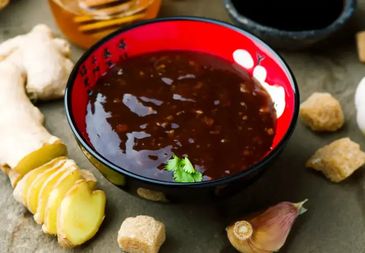 Miseczka z aromatycznym sosem teriyaki, obok świeży imbir, czosnek i brązowy cukier.