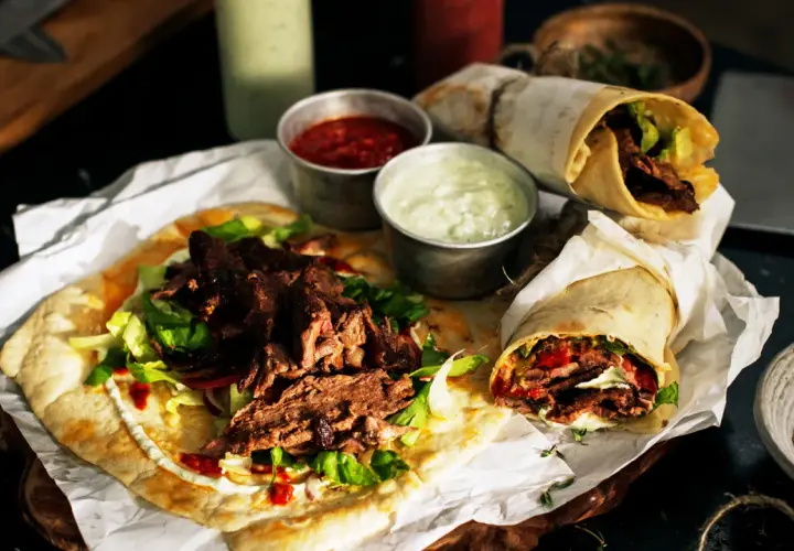 Pyszny lawasz kebab z soczystym mięsem, świeżą sałatą i sosami. Dwa zawinięte w papier i jeden otwarty na płaskim chlebie.