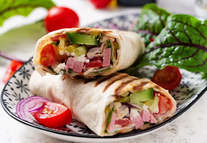Pyszna tortilla z szynką i serem, pełna świeżych warzyw, podana na talerzu z pomidorkami i sałatą.