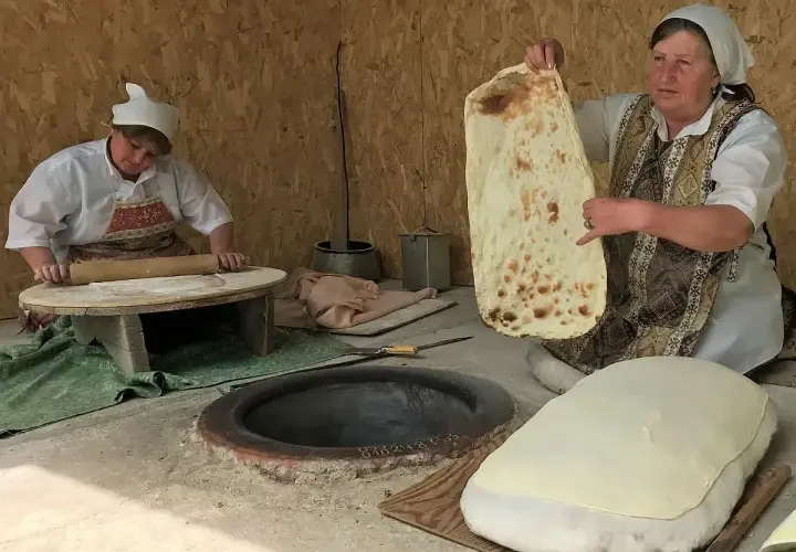 Kobieta pokazuje, co to jest lawasz – tradycyjny ormiański chleb. Obok druga kobieta wałkuje ciasto.