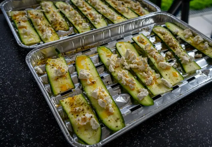 Półplasterki cukinii z serem feta i przyprawami, gotowe do grillowania.