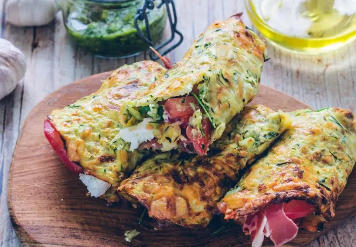 Złociste tortilla z cukinii, nadziewane serem, pomidorami i szynką, prezentowane na drewnianej desce.