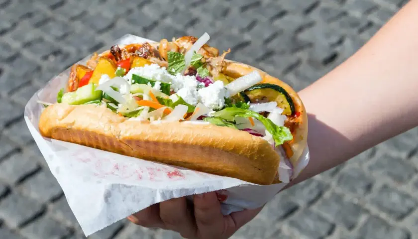 Kebab w bułce z kurczakiem i wołowiną, z warzywami i serem feta, trzymany w dłoni.