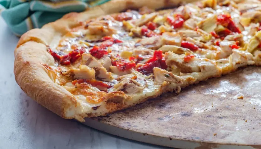 Kawałek domowej pizzy z kurczakiem i suszonymi pomidorami na kamieniu.