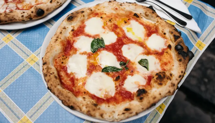 Pizza Margherita z roztopioną mozzarellą i bazylią na niebiesko-żółtym obrusie.