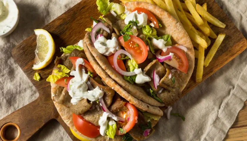 Pyszny kurczak gyros w picie z pomidorami, cebulą, sałatą i sosem. Obok frytki i cytryna.