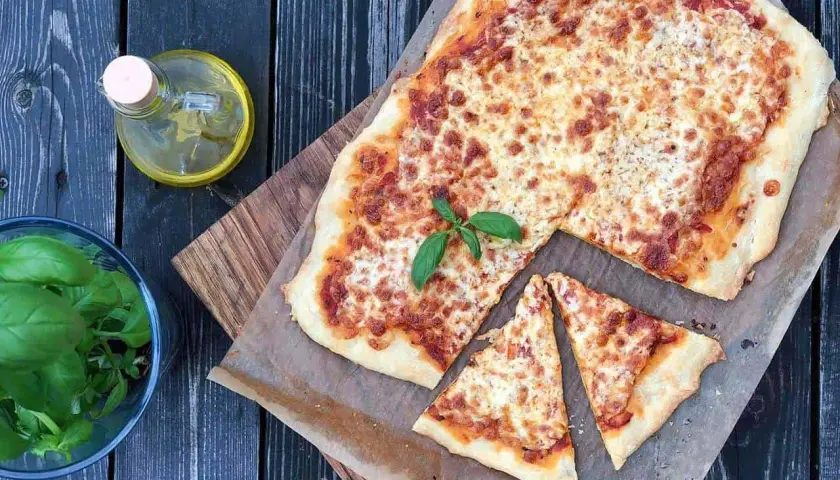 Pyszna margarita pizza z roztopionym serem i świeżą bazylią, obok butelka oliwy i miseczka ziół.