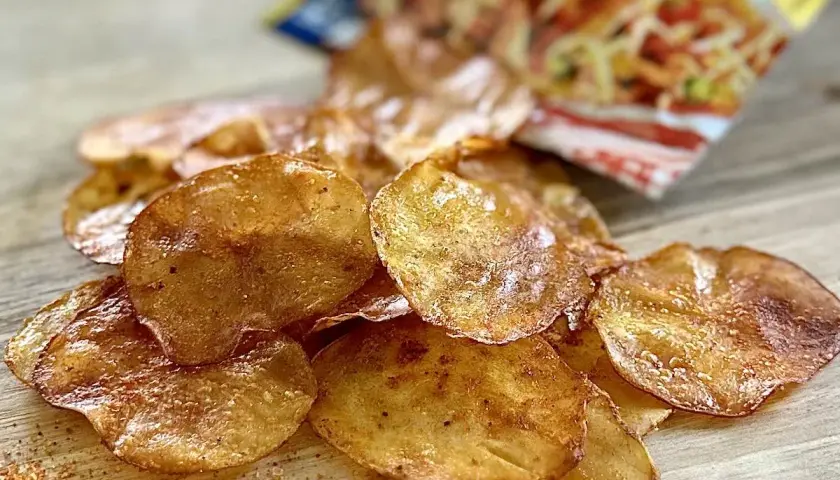 Chrupiące, złociste domowe chipsy z piekarnika, posypane przyprawami, leżą na drewnianym blacie obok otwartej paczki.
