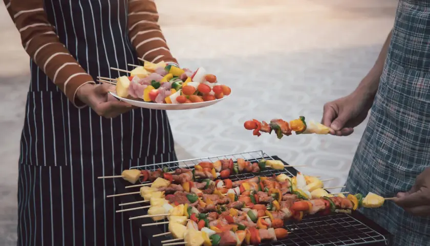 Ludzie grillują szaszłyki z mięsem i warzywami na grillu.