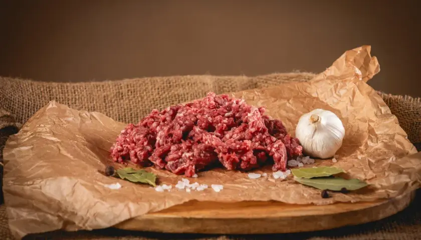 Świeże, mielone mięso wołowe, idealne na soczyste burgery. Obok czosnek, sól, liście laurowe i pieprz.
