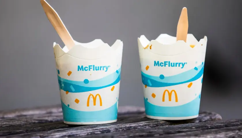 Dwa kubeczki McFlurry pistacjowe z drewnianymi łyżeczkami na drewnianym blacie.