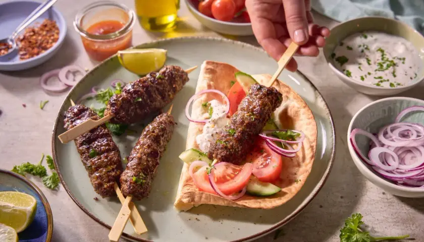 Pyszny, soczysty turecki kebab na talerzu z dodatkami: pitą, warzywami i jogurtowym sosem. Idealny na letni wieczór.