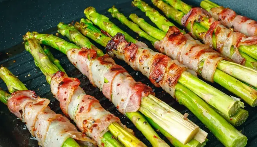 Zielone szparagi owinięte w boczek, grillowane na patelni. Pyszne szparagi z grilla gotowe do podania.