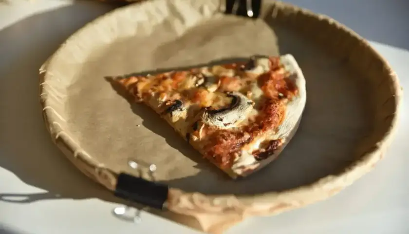 Kawałek pizzy z pieczarkami na papierowym talerzu. Zastanawiasz się nad pizza kcal?