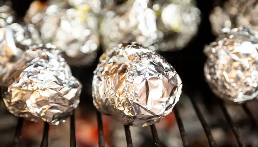 Ziemniaki z grilla zawinięte w folię aluminiową, piekące się nad żarem.