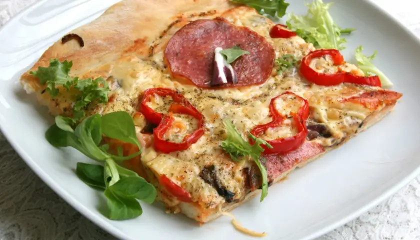Kawałek pizzy z salami, papryką i serem na białym talerzu.