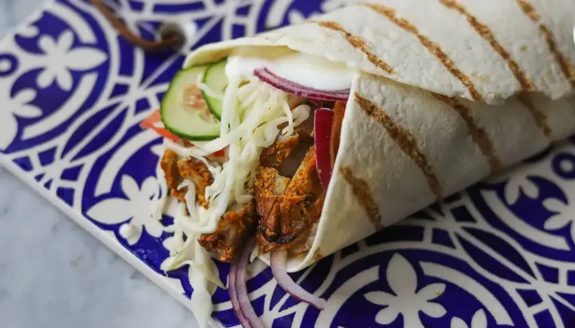 Pyszny kebab w picie z soczystym mięsem, chrupiącą kapustą, pomidorem, ogórkiem i czerwoną cebulą, podany na ozdobnym talerzu.