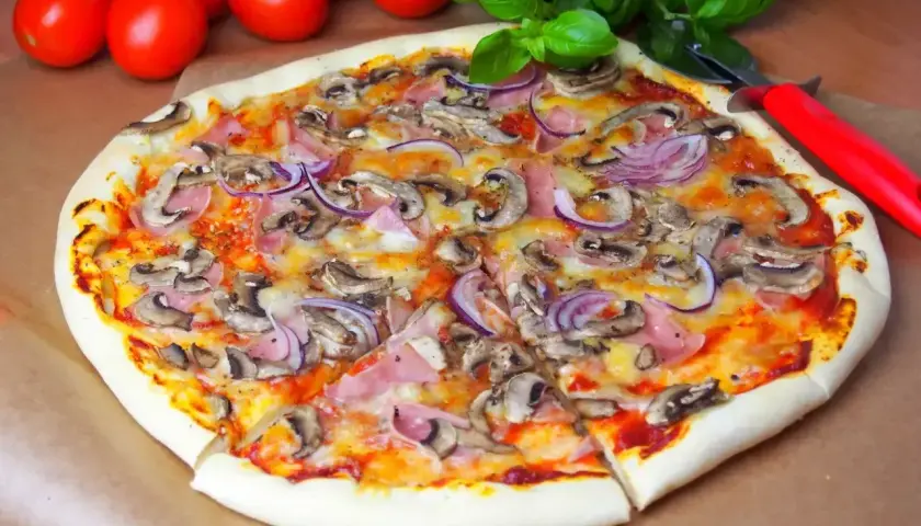 Pyszna pizza capriciosa z pieczarkami, szynką i czerwoną cebulą, gotowa do pokrojenia.