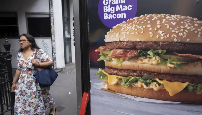 Reklama Grand Big Mac Bacon. Kobieta w kwiecistej sukience mija billboard z apetycznym burgerem.
