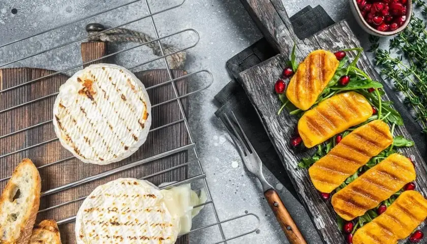 Dwa krążki sera camembert na grillu, jeden lekko roztopiony, obok grzanki i grillowane kawałki dyni z pestkami granatu.