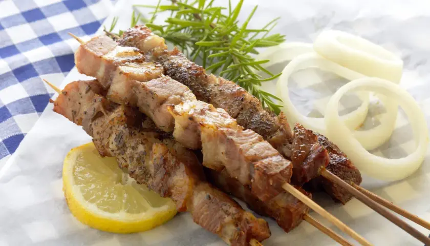 Aromatyczne souvlaki na patyczkach, podane z plasterkiem cytryny, gałązką rozmarynu i krążkami cebuli.