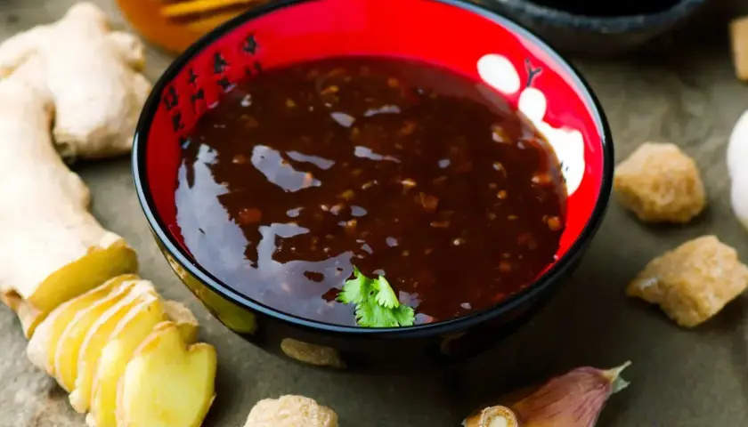 Miseczka z aromatycznym sosem teriyaki, obok świeży imbir, czosnek i brązowy cukier.