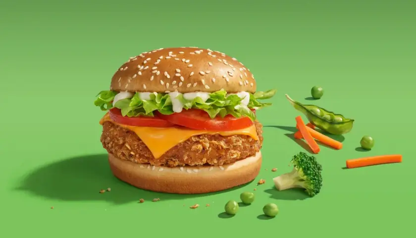 Pyszny wege burger McDonald's z chrupiącym kotletem, serem, pomidorem i sałatą. Obok świeże warzywa: groszek, marchewka i brokuł.