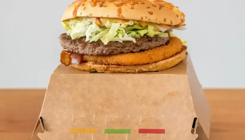 Drwal z chrzanem, czyli soczysty burger z chrupiącą panierką i wołowiną, na papierowym opakowaniu.