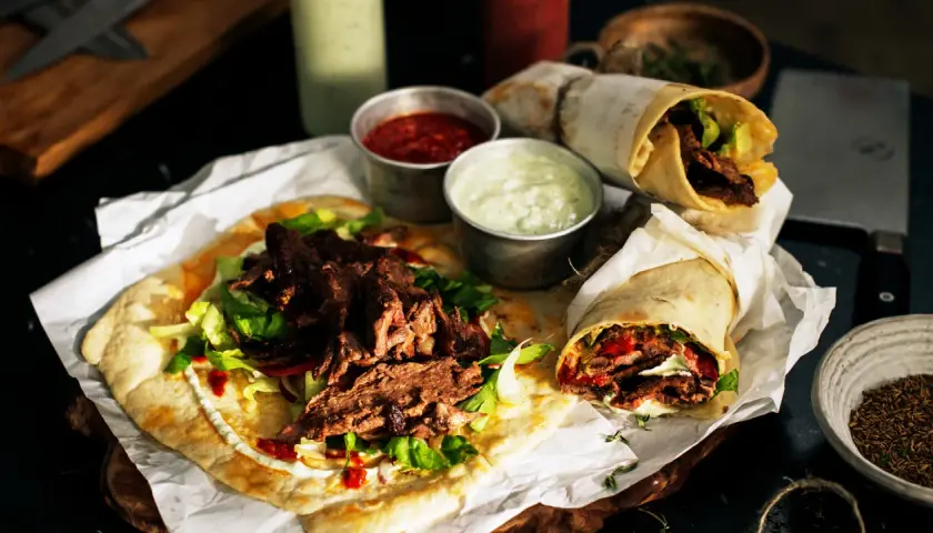 Pyszny lawasz kebab z soczystym mięsem, świeżą sałatą i sosami. Dwa zawinięte w papier i jeden otwarty na płaskim chlebie.
