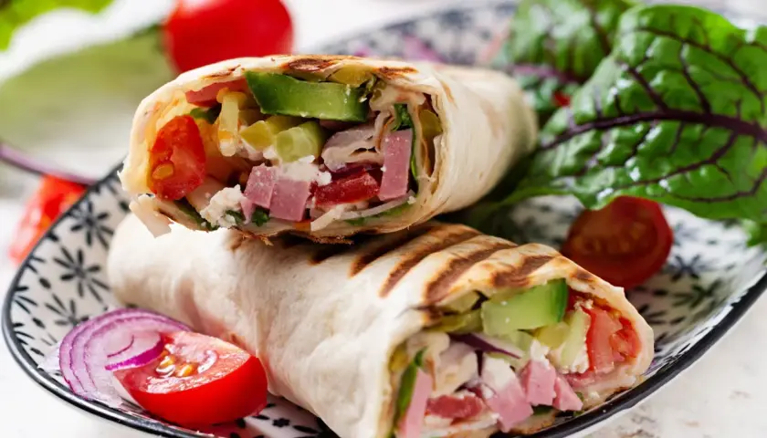 Pyszna tortilla z szynką i serem, pełna świeżych warzyw, podana na talerzu z pomidorkami i sałatą.