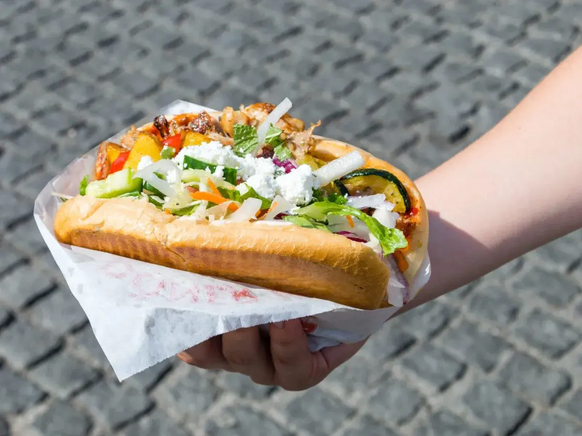 Kebab w bułce z kurczakiem i wołowiną, z warzywami i serem feta, trzymany w dłoni.