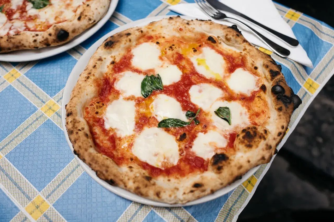 Pizza Margherita z roztopioną mozzarellą i bazylią na niebiesko-żółtym obrusie.
