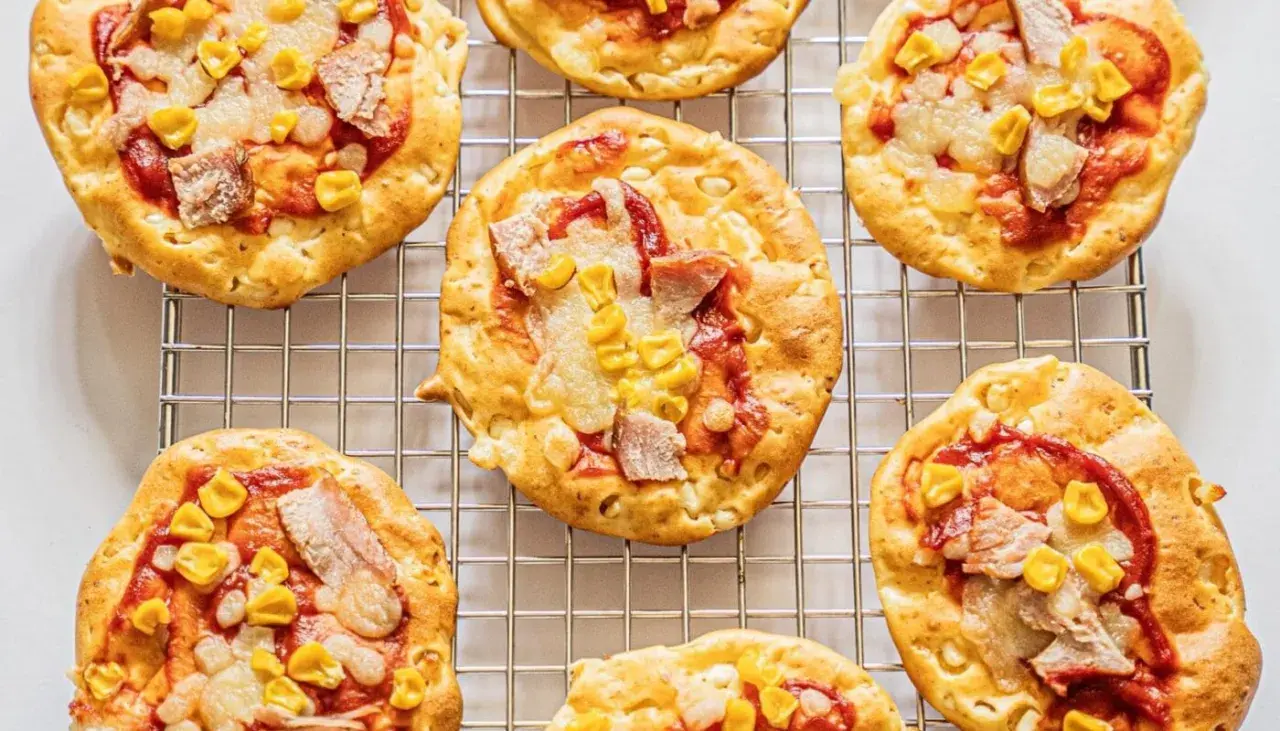 Mini pizze z serka wiejskiego, z kukurydzą i kawałkami mięsa, na metalowej kratce.